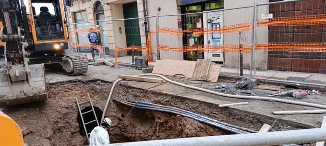 Escavatore e pozzo di scavo con un tecnico su una scala in un cantiere urbano