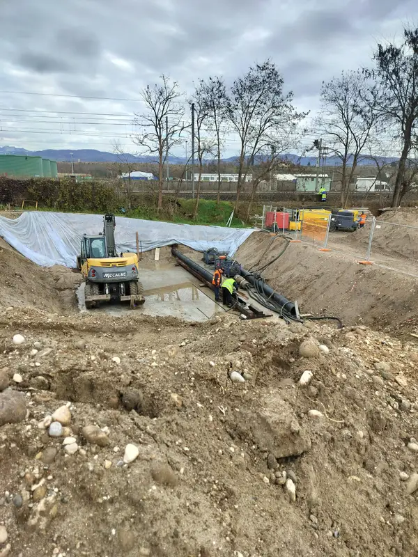 Pozzo di spinta per spingitubo a Pescantina: tubazione in acciaio, centralina idraulica e squadra al lavoro, con la linea ferroviaria sullo sfondo