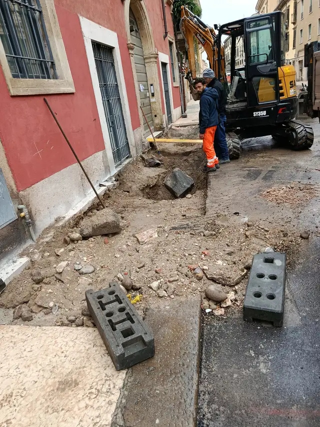 Squadra e mini-escavatore in una via del centro storico
